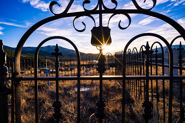 Fenced in area at old cemetery captured during golden hour with sun star shining through elements of the fence and grave stones in background.