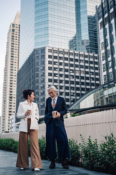 Business colleagues walking on city street, carrying coffee and talking, enjoying a break outdoors