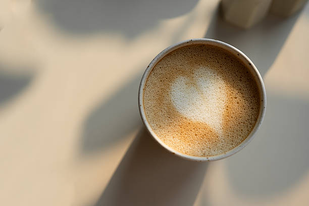 Top view of a cup of coffee with heart-shaped latte art on a light surface. Suitable for concepts related to coffee, love, cafes, and morning routines.