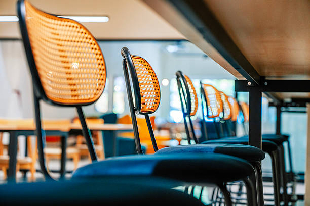 Low-angle close-up of woven-back chairs lined along a shared counter in a bright contemporary coworking, café-style, or hospitality interior with modern design details, Penang