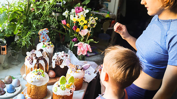 In the kitchen, a boy, brother, and older sister are decorating Easter baked goods