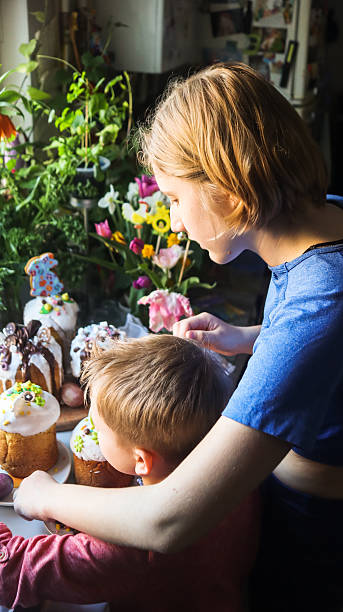 In the kitchen, a boy, brother, and older sister are decorating Easter baked goods