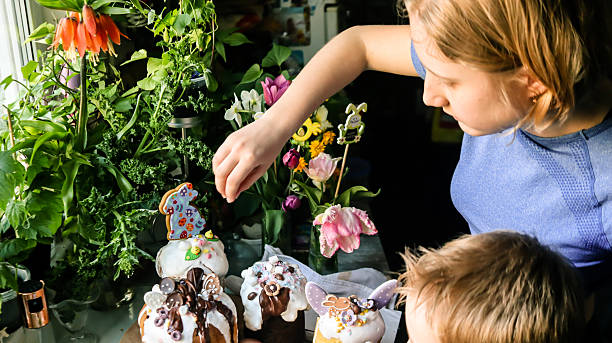 In the kitchen, a boy, brother, and older sister are decorating Easter baked goods