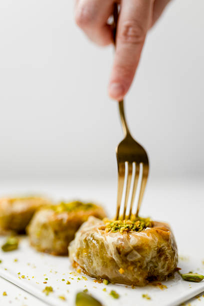 Fork picking pistachio baklava pastry on white plate in elegant food composition