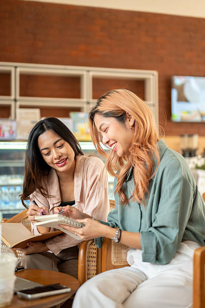 Asian woman student discussing with friend while working on group project or study together in cafe.