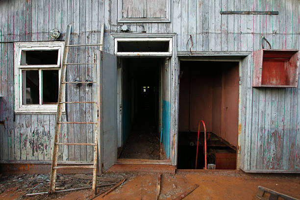 Exploring an abandoned wooden structure with a weathered facade and open entrances in a remote location during daylight