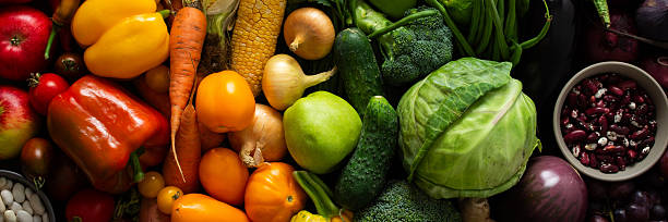 Fresh vegetables and fruits are arranged on a dark surface, showing a variety of colors and shapes. This was captured after a recent harvest from a local farm, banner