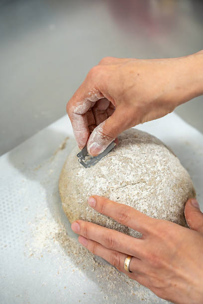Baker scoring sourdough bread dough with razor blade