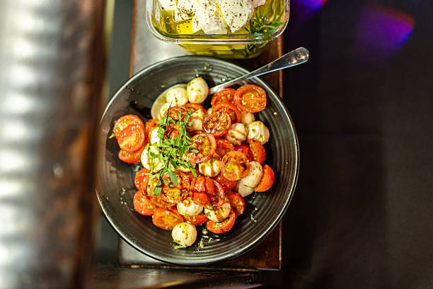 Caprese Salad With Cherry Tomatoes, Mozzarella Balls and Fresh Basil Garnish on Black Plate