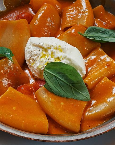 Paccheri pasta with tomato sauce topped with fresh burrata cheese and basil leaves. Italian comfort food dish with creamy burrata, olive oil, and rich tomato sauce, close-up gourmet pasta plating.