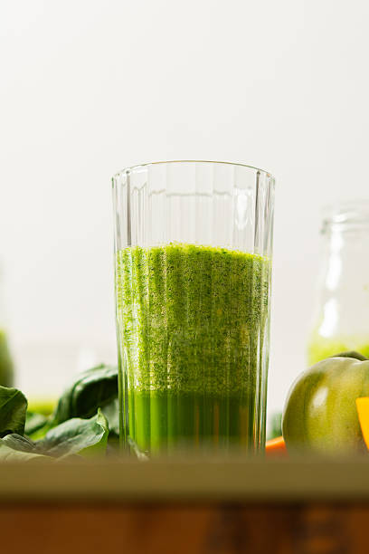 Fresh juice is made using spinach, chard, and broccoli along with oranges and tangerines. A glass of green juice sits by fresh ingredients on a clean kitchen counter