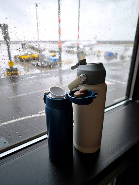 Reusable water bottles on a windowsill at Berlin Airport, overlooking the tarmac in the rain.