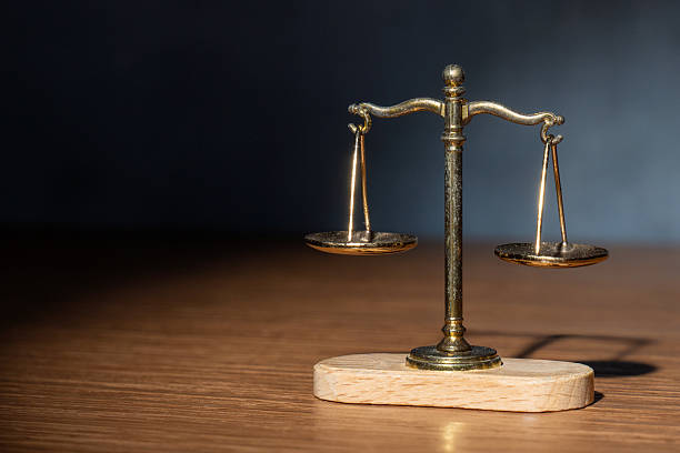 A vintage scale of justice standing on a wooden surface with dramatic side lighting. Concept for legal systems, court verdicts, weight of evidence, equality, and law.