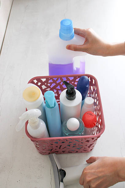 Top view of a hand holding a transparent plastic bottle and placing it into a basket with other empty containers. The image represents recycling, waste sorting, and responsible plastic disposal. It highlights environmental awareness, sustainability, and eco-friendly household habits.
