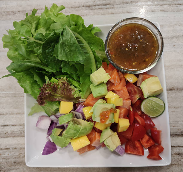 Fresh Salmon Thai Style Salad with Avocado, Mango, Bell Peppers, Lettuce, Lime, and Spicy Thai Dressing on a White Plate