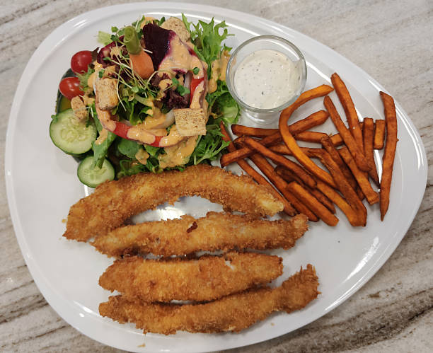 Crispy Breaded Chicken Strips Served with Fresh Garden Salad, Sweet Potato Fries, and Creamy Dipping Sauce on a Modern White Plate