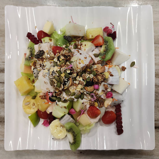 Fresh Mixed Fruit Salad with Kiwi, Dragon Fruit, Apple, Cherry Tomatoes, and Granola Topping Served on a White Plate