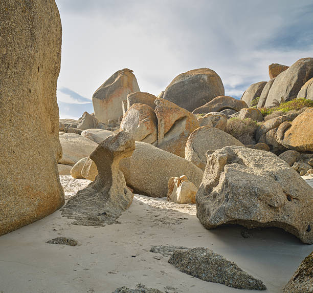 A serene coastal scene in the Western Cape features large weathered granite boulders scattered across pale sand, with a bright sky above. The rugged rocks create textures of orange and gray, evoking a remote natural landscape near Cape Town. Ideal for nature, travel, and outdoors themes.