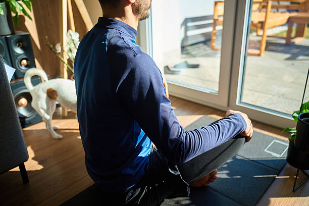 Man sitting cross legged on mat near window during home meditation