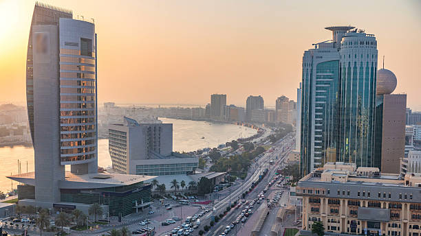 Dubai creek landscape at sunset timelapse with boats and yachts and modern buildings with traffic on the road and car parking. Aerial top view from above with orange sky