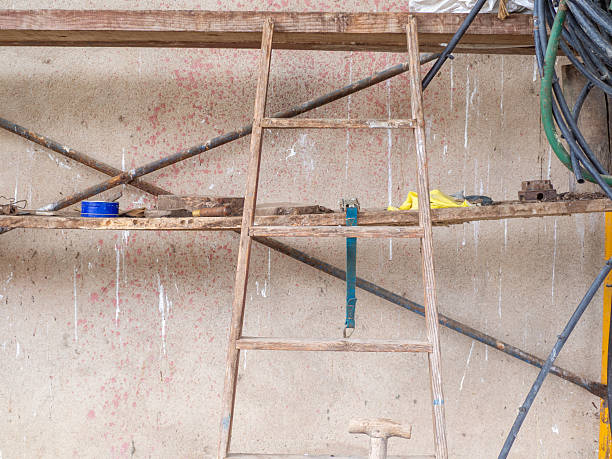Old wooden ladder standing against a dirty wall with construction tools on scaffolding