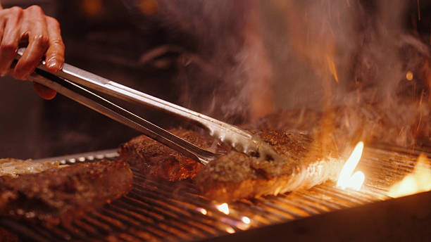 Professional chef grilling beef steak on a hot grill in a restaurant kitchen, preparing gourmet food
