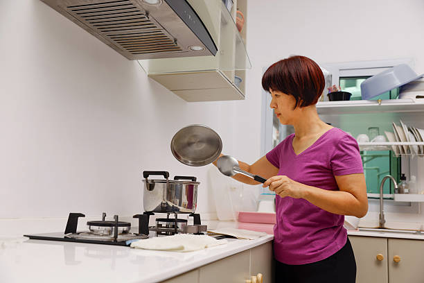 Senior asian housewife open a lid of cooking pot in kitchen.