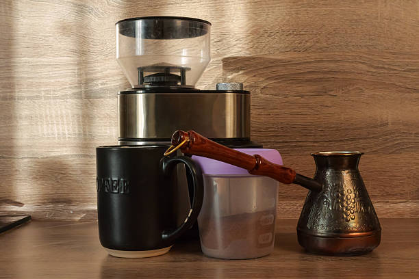 Coffee Grinder Cezve Mug Copper Jar On Wooden Counter Bathed In Warm Side Light Closeup Of Specialty Coffee Tools With Bean Hopper, Measuring Pitcher And Glass Jar For Grounds, Barista Practice Scene