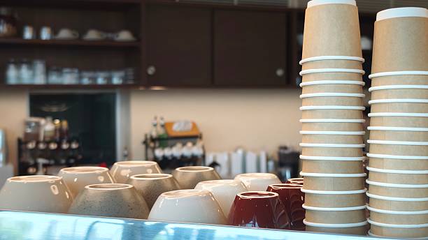 Stacks upside down empty brown takeaway disposable coffee cardboard cups on the coffee machine in the cafe.