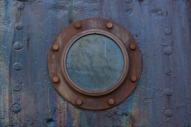 Close-up of a rusty porthole on an old metal ship hull.; Industrial background with round window and weathered metal surface.