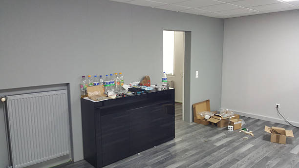 An unorganized office space with cardboard boxes, plastic bottles, and various items strewn across the floor and furniture