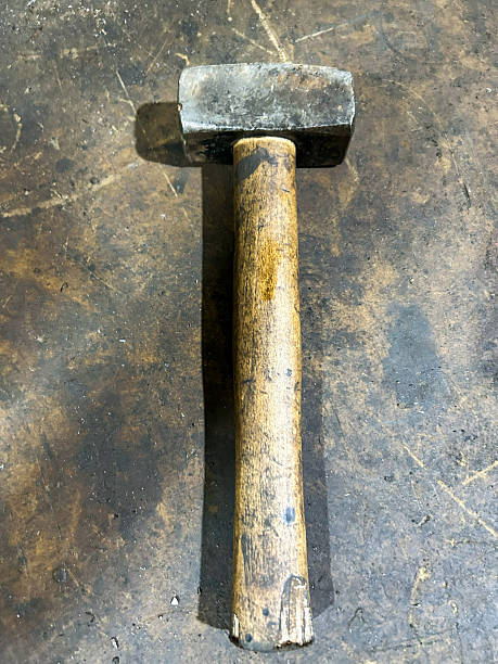 Heavy mallet hammer with a wooden handle resting on a worn industrial surface