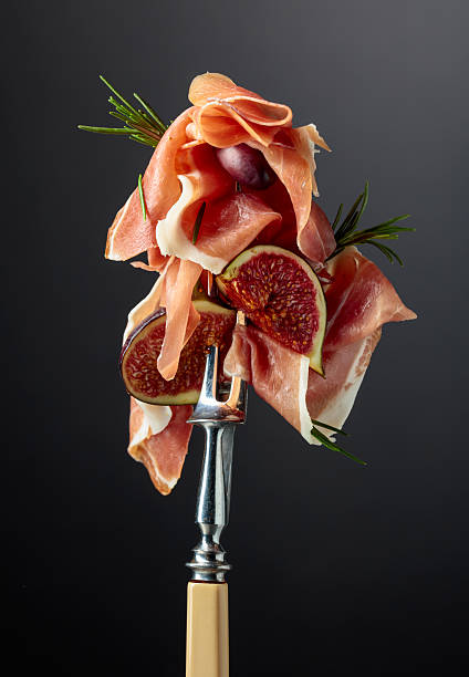Prosciutto with figs, rosemary, and red olives on a fork.