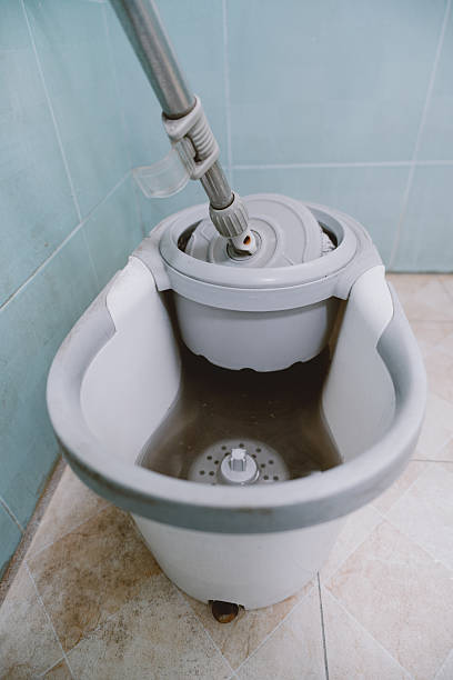 White spin mop bucket with dirty water in tiled bathroom, modern cleaning tool for home use