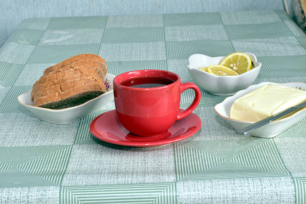 A porcelain cup of tea, butter and sliced ​​bread stand on the table.
