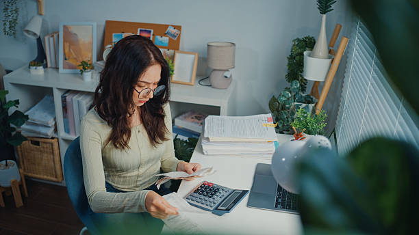 Young woman reviewing receipts and bills, feeling stressed while planning her personal budget with laptop and paperwork on the desk in home office.