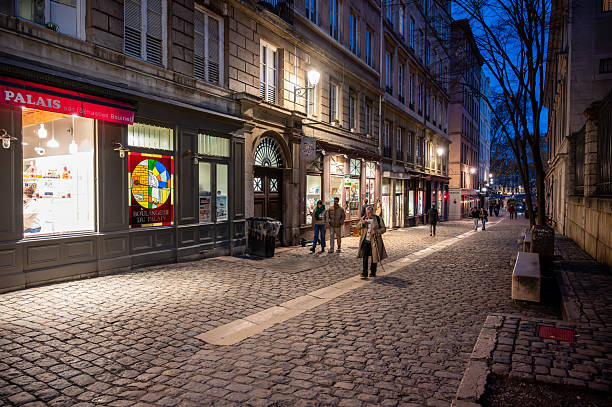 Lyon, france. December 29, 2023. Couple strolling a charming cobblestone street in vieux lyon at dusk, warm shop lights and lanterns illuminating historic faÃ§ades