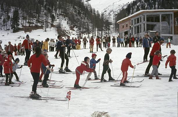 Switzerland (exact location unknown), 1968. Children's ski school with ski instructors, on a slope in the Swiss Alps. The parents stand in the background and watch.