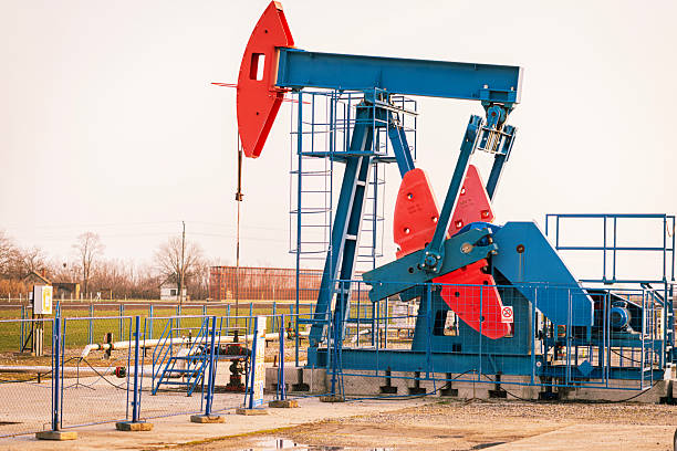 Silhouette of an operating oil pumpjack extracting crude oil from the ground during sunset. Warm golden light creates a dramatic industrial landscape, symbolizing petroleum production, energy resources, fossil fuels, and the global oil industry. Suitable for themes of energy economy, natural resources, and industrial infrastructure.