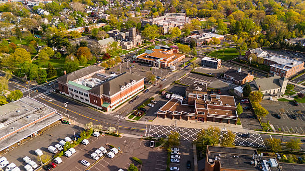 Aerial view of commercial district in Summit, New Jersey during spring afternoon. Buildings, parking lots, and streets are visible, with residential neighborhoods and trees in the background.