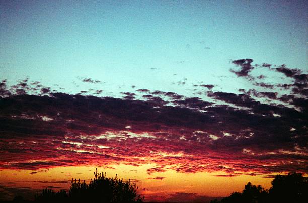 Photographie d’un coucher de soleil capturée sur film Kodak ColorPlus 200 avec un appareil argentique Canon Sure Shot. L’image montre les couleurs chaudes du sunset avec des tons orange et dorés reflétés dans le ciel. La photo a été développée et scannée à la maison, mettant en valeur le grain naturel et l’esthétique authentique de la photographie argentique.