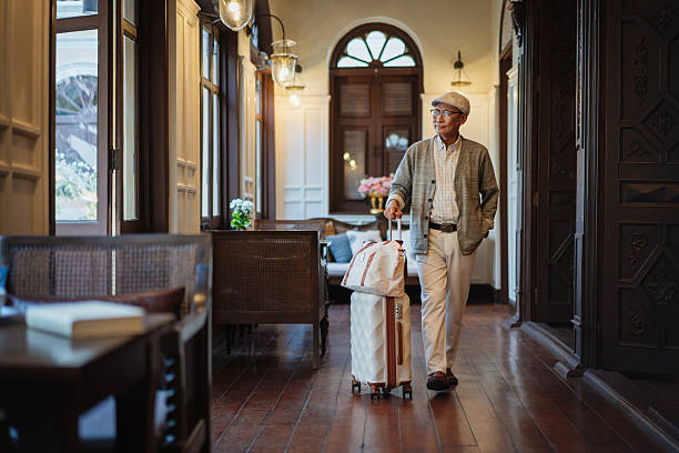 Mature man walking through an elegant hotel corridor with luggage, arriving for a relaxing stay.