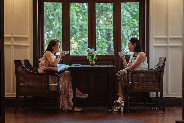 Two elegant women are enjoying a relaxing conversation while drinking coffee in a stylish cafe.
