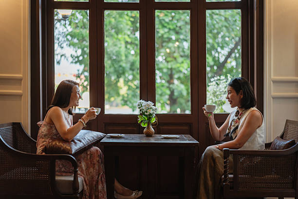 Two elegant women are enjoying a relaxing conversation while drinking coffee in a stylish cafe.
