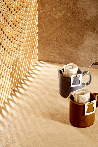 High-angle shot of coffee being poured into drip bags with rhythmic shadows.