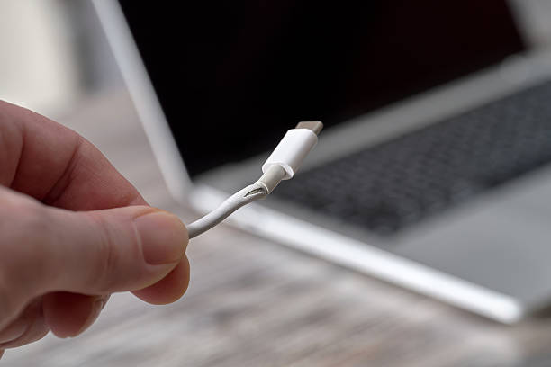 A man holds a damaged laptop charger cable in his hand.