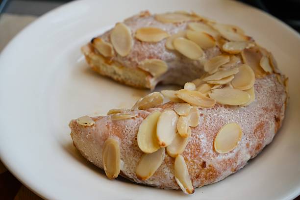 Partially eaten glazed ring doughnut topped with toasted almond slices on white plate,