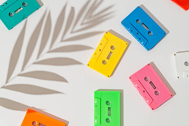 Colorful retro audio cassette tapes flat lay with palm leaf shadow on white background. 80s 90s nostalgia music background. Old summer hits idea backdrop. Light and shadow.