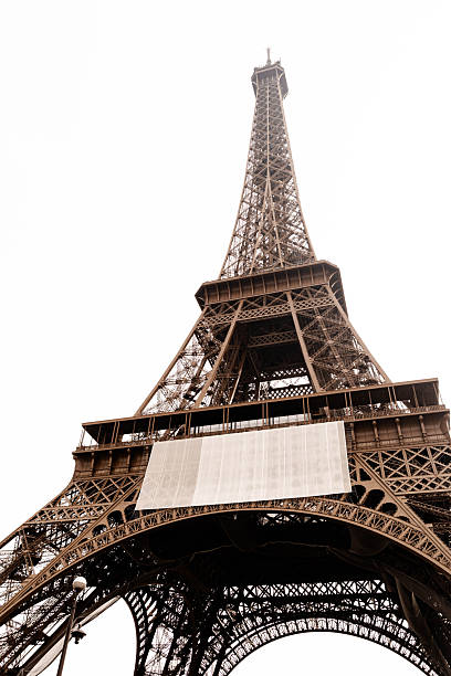 Iconic Eiffel Tower captured from a dramatic low angle, showcasing intricate iron architecture against a pale Paris sky. Timeless landmark symbolizing travel, romance, and European culture