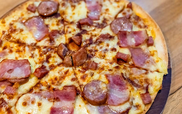 Bacon and sausage pizza with melted cheese on a wooden board, close-up. Rich textures and crispy toppings create a delicious fast food and restaurant food concept